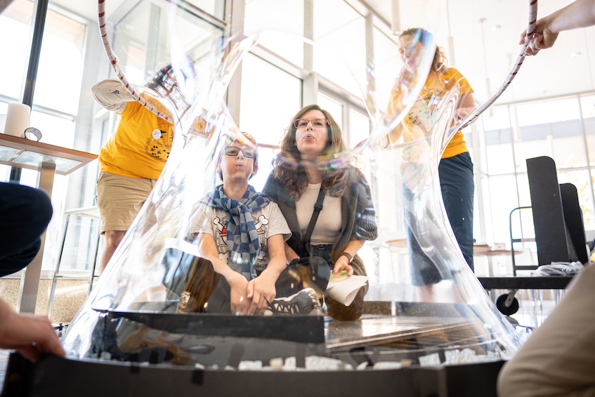 “A Seat at the Surface Circus” — At the Discovery Expo, the outreach group from the department of chemistry at UW–Madison gives two attendees the opportunity to join the “Surface Circus,” as they create a giant bubble chamber to showcase the power of surface tension. (Photo by Romulo Ueda Photography)