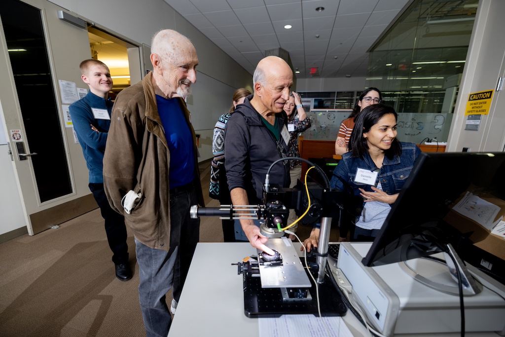 Postdoctoral Fellow Danielle Desa assists attendees with using a specialized instrument for eye exams to image the grooves of their fingerprints.