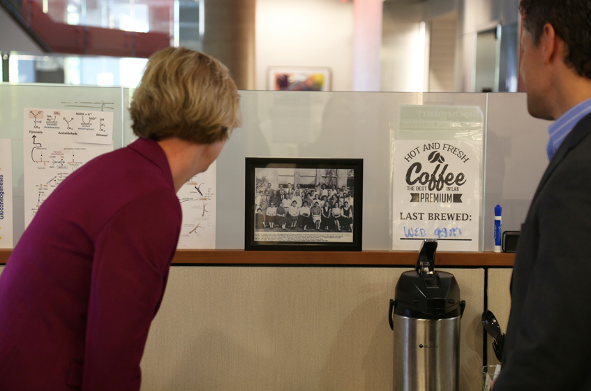 Senator Tammy Baldwin examines a picture of her late grandfather's (David E. Green) research lab members. Dave Pagliarini (right), leads research at the Morgridge Institute that builds upon the research legacy of Baldwin's grandfather. 