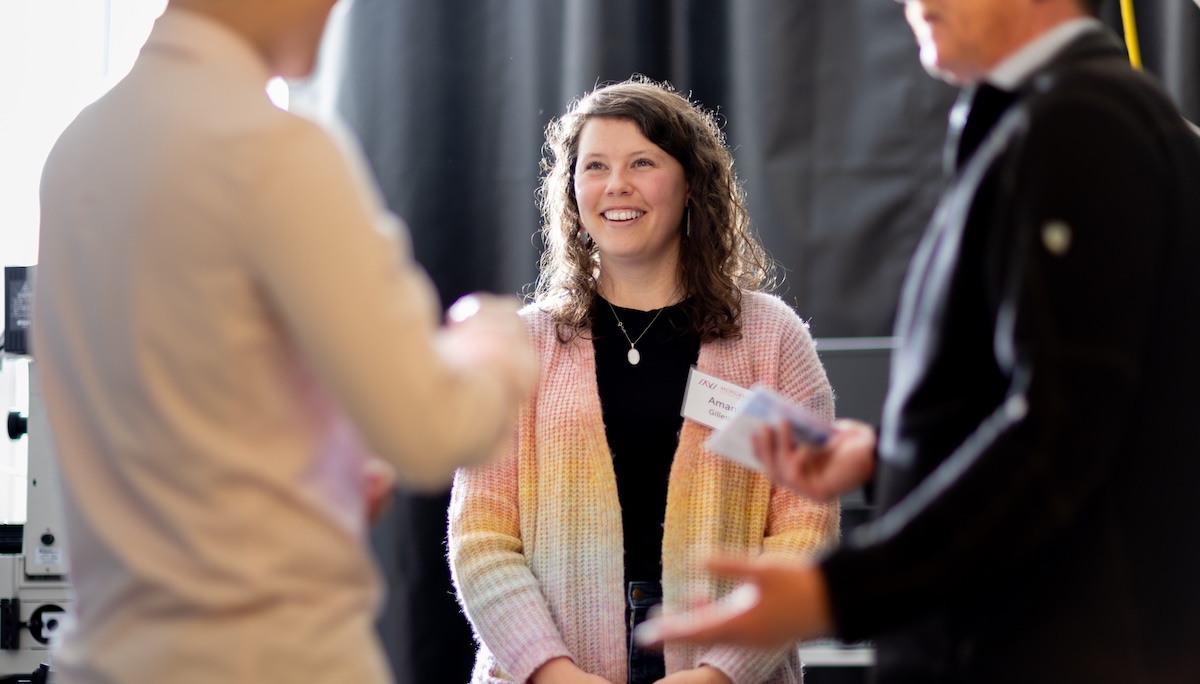 A woman stands smiling in conversation with colleagues.