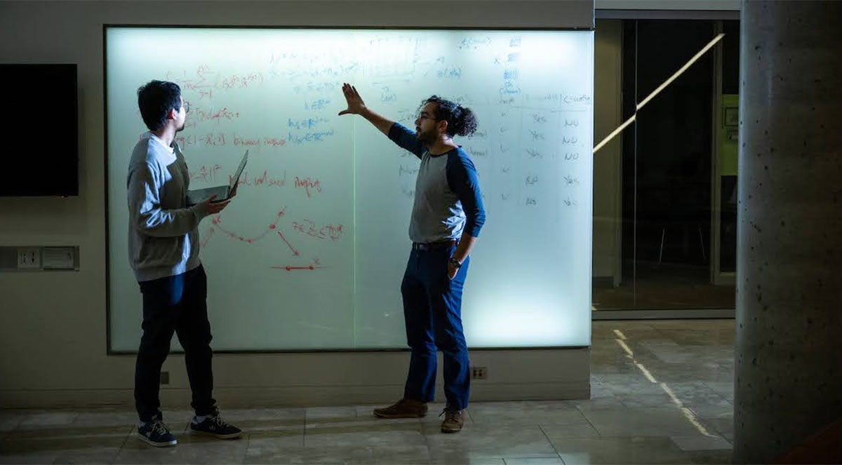 Two people standing in front of an illuminated whiteboard.